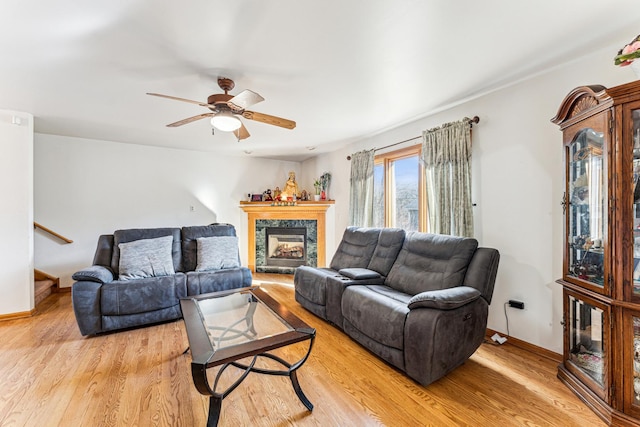 living area with light wood-type flooring, stairs, a premium fireplace, and ceiling fan