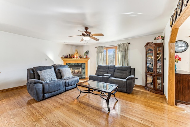 living area with ceiling fan, a fireplace, light wood-style flooring, and baseboards