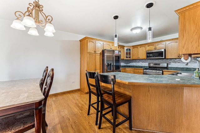 kitchen with a peninsula, a sink, appliances with stainless steel finishes, backsplash, and light wood finished floors