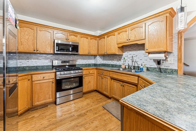 kitchen with stainless steel appliances, a sink, light wood-style flooring, and decorative backsplash