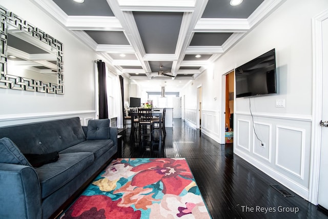 living area featuring beam ceiling, dark wood finished floors, coffered ceiling, and wainscoting