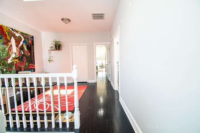 hall with an upstairs landing, visible vents, baseboards, and wood-type flooring