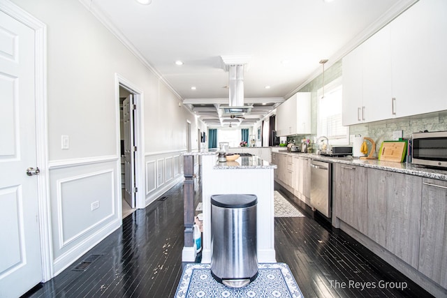 kitchen featuring a wainscoted wall, dark wood finished floors, a center island, stainless steel appliances, and crown molding