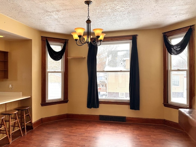 unfurnished dining area with an inviting chandelier, dark hardwood / wood-style floors, and a textured ceiling