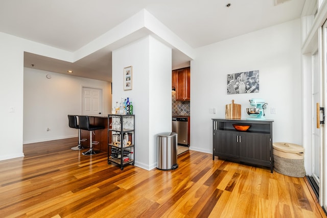 bar with decorative backsplash, dishwasher, and light wood-type flooring