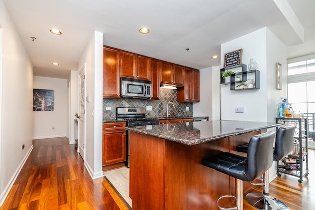 kitchen featuring appliances with stainless steel finishes, a kitchen island, dark stone counters, dark hardwood / wood-style floors, and tasteful backsplash