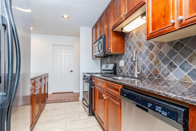 kitchen with stainless steel appliances, sink, tasteful backsplash, light tile patterned floors, and dark stone counters