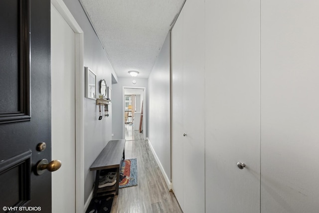 corridor with light wood-type flooring and a textured ceiling