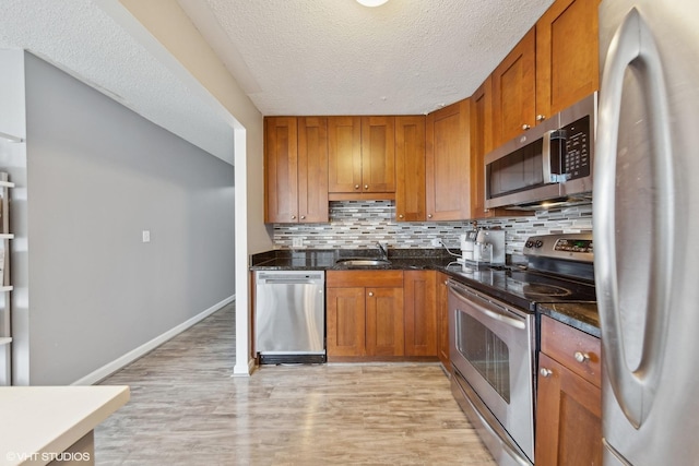 kitchen featuring stainless steel appliances, light hardwood / wood-style floors, sink, a textured ceiling, and decorative backsplash