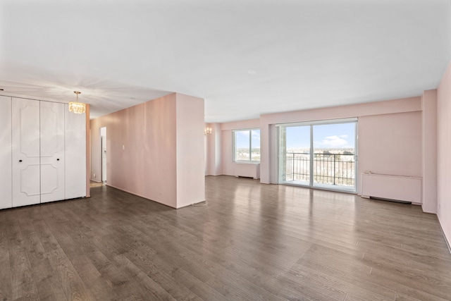 unfurnished living room featuring a chandelier, radiator heating unit, and wood finished floors