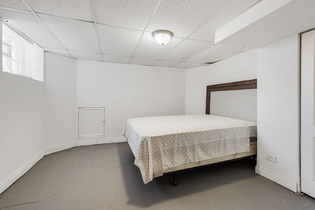 bedroom with finished concrete flooring, baseboards, and a drop ceiling