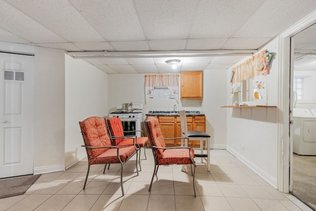 living area featuring washer / dryer, a paneled ceiling, baseboards, and light tile patterned floors