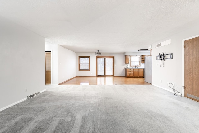 unfurnished living room featuring a textured ceiling, baseboards, visible vents, and light colored carpet