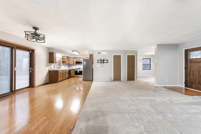 unfurnished living room featuring a textured ceiling, light wood finished floors, and baseboards