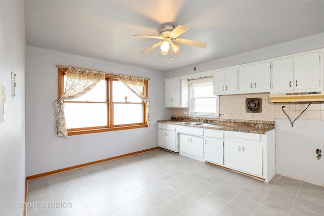 kitchen with baseboards, white cabinetry, backsplash, ceiling fan, and a sink