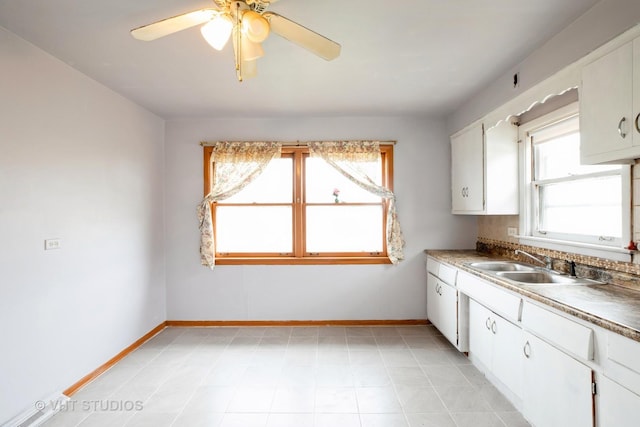 kitchen featuring white cabinetry, a sink, a ceiling fan, and baseboards