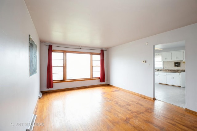 empty room with light wood finished floors, visible vents, and baseboards