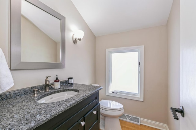 half bath with toilet, wood finished floors, vanity, visible vents, and baseboards