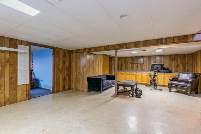 living area with a drop ceiling and wooden walls