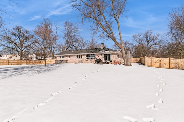 snow covered back of property featuring a chimney and fence