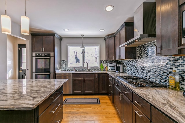 kitchen with wall chimney range hood, appliances with stainless steel finishes, pendant lighting, and a sink