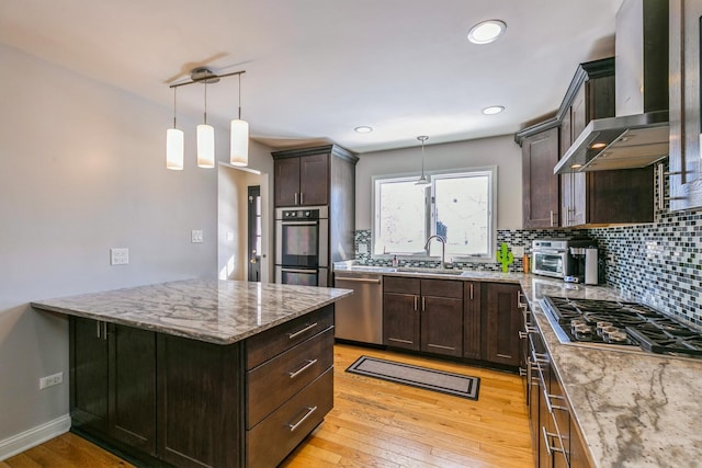 kitchen featuring appliances with stainless steel finishes, a sink, wall chimney range hood, and light stone counters