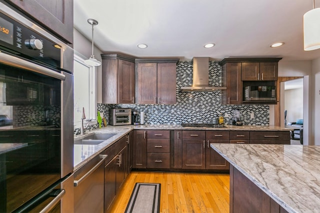 kitchen featuring light stone counters, stainless steel appliances, a sink, wall chimney range hood, and decorative light fixtures