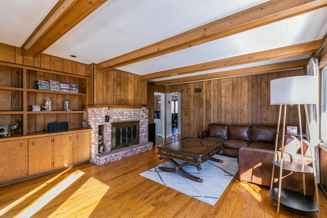 living room featuring a brick fireplace, light wood-style flooring, wooden walls, and beamed ceiling