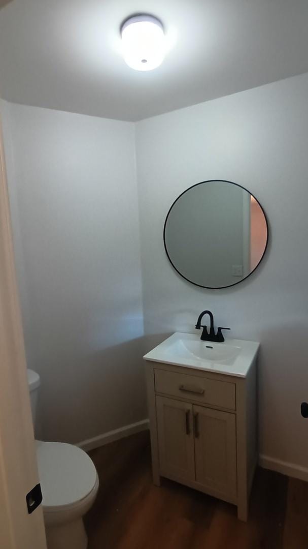 half bathroom with toilet, wood finished floors, vanity, and baseboards