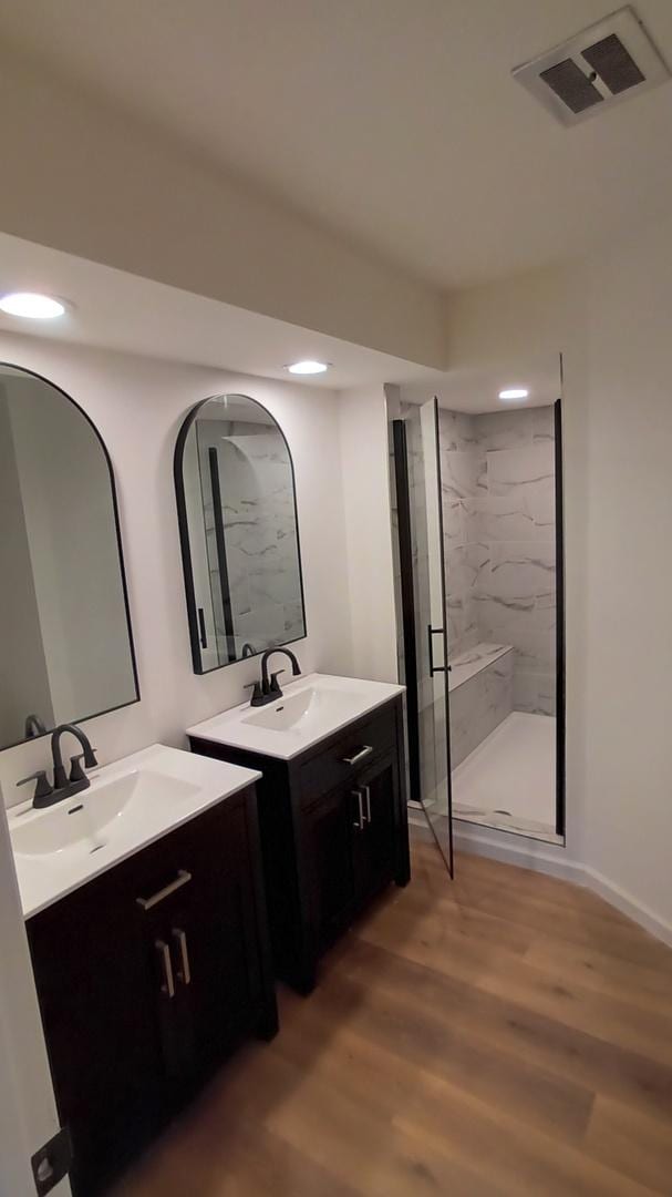 bathroom with a marble finish shower, visible vents, a sink, and wood finished floors