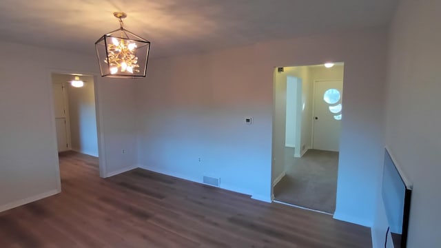 spare room with a chandelier, wood finished floors, visible vents, and baseboards