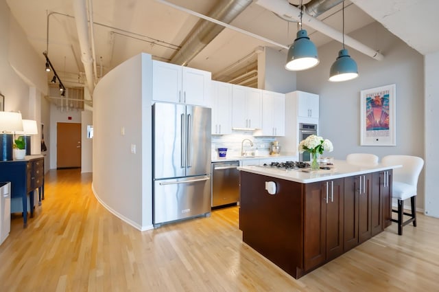 kitchen with light countertops, a high ceiling, white cabinets, stainless steel appliances, and a sink