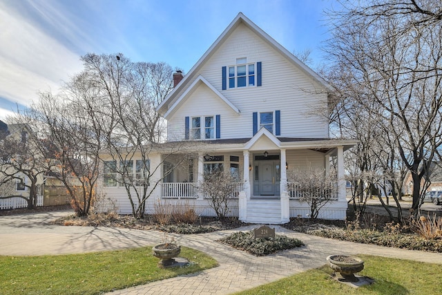 view of front of home with driveway, a chimney, and a porch