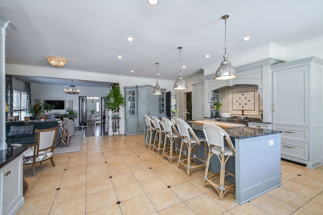 kitchen with light tile patterned floors, crown molding, dark stone countertops, and an inviting chandelier