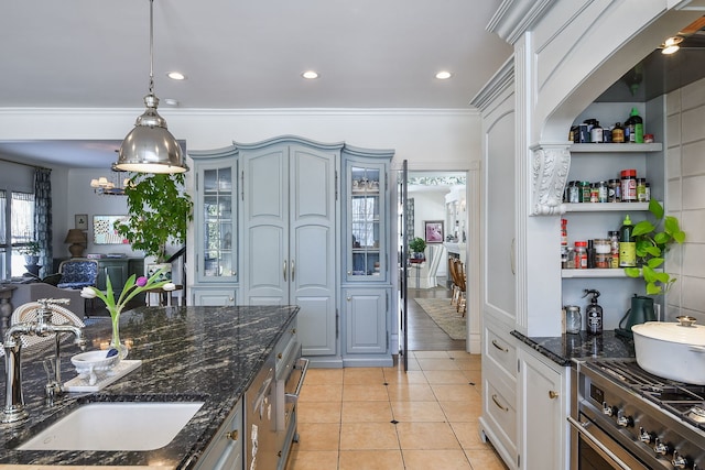 kitchen featuring light tile patterned flooring, a sink, hanging light fixtures, stainless steel range, and glass insert cabinets