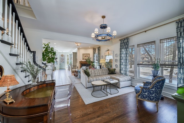 living area featuring a fireplace, stairway, ornamental molding, wood finished floors, and a chandelier