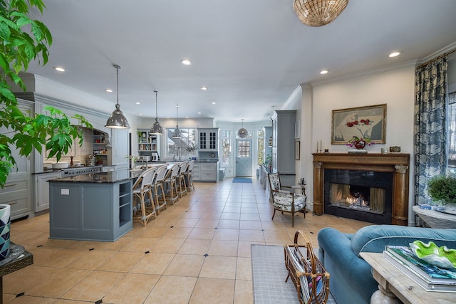 kitchen featuring light tile patterned floors, gray cabinets, ornamental molding, a lit fireplace, and a kitchen bar