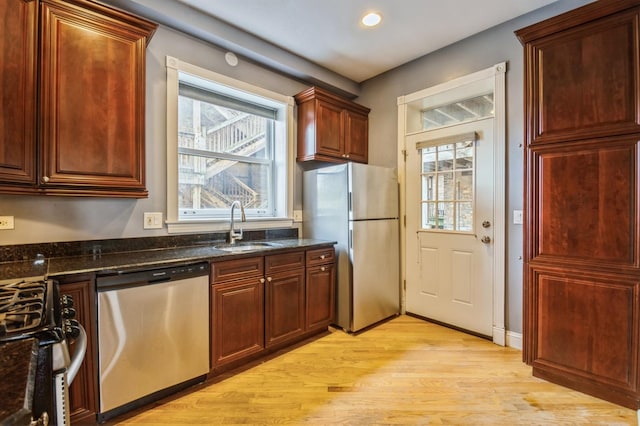 kitchen featuring appliances with stainless steel finishes, a healthy amount of sunlight, a sink, and light wood finished floors