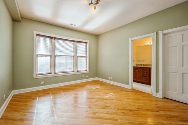 unfurnished bedroom featuring ensuite bath, light wood-style floors, baseboards, and visible vents