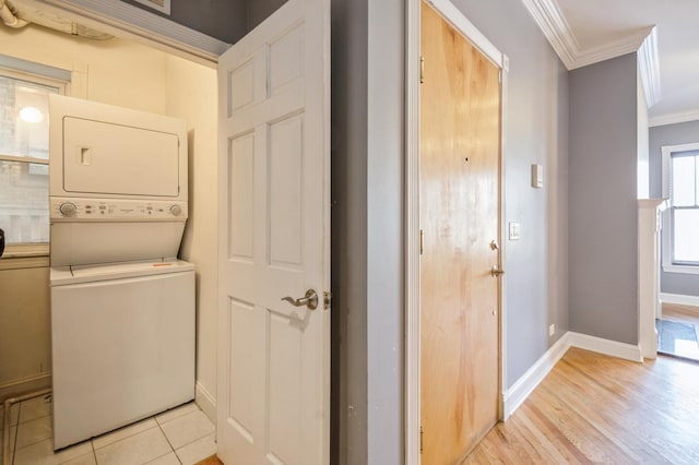 clothes washing area featuring stacked washer and dryer, laundry area, baseboards, crown molding, and light wood-style floors