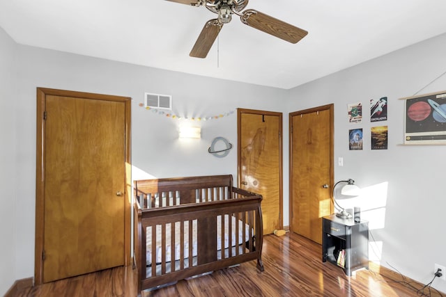 bedroom with ceiling fan, a crib, wood finished floors, and visible vents