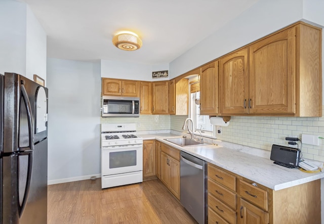 kitchen featuring light wood-style flooring, stainless steel appliances, a sink, light countertops, and backsplash