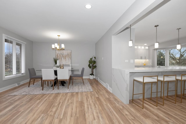 dining area with an inviting chandelier, light hardwood / wood-style floors, and indoor bar