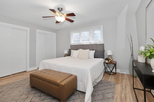 bedroom featuring ceiling fan, light hardwood / wood-style floors, and two closets