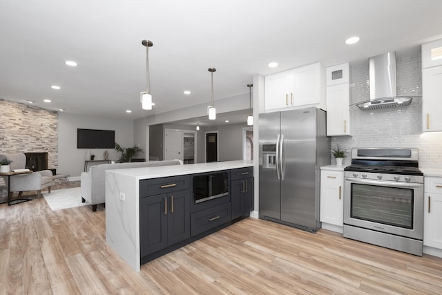 kitchen featuring wall chimney range hood, appliances with stainless steel finishes, hanging light fixtures, white cabinets, and kitchen peninsula