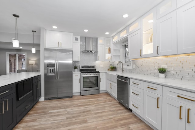 kitchen with white cabinetry, hanging light fixtures, stainless steel appliances, light stone counters, and wall chimney exhaust hood