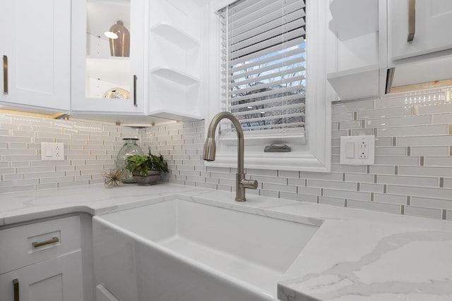 interior details featuring white cabinetry, sink, decorative backsplash, and light stone countertops