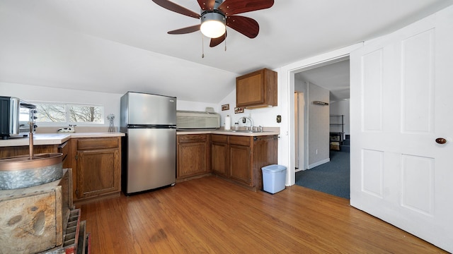 kitchen with sink, stainless steel refrigerator, ceiling fan, vaulted ceiling, and light wood-type flooring