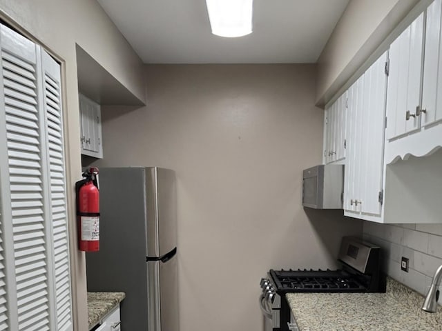 kitchen featuring appliances with stainless steel finishes, white cabinets, light stone counters, and decorative backsplash