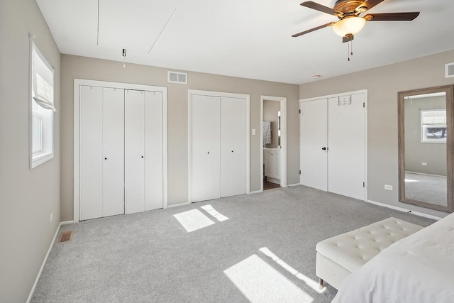 carpeted bedroom featuring connected bathroom, two closets, and ceiling fan